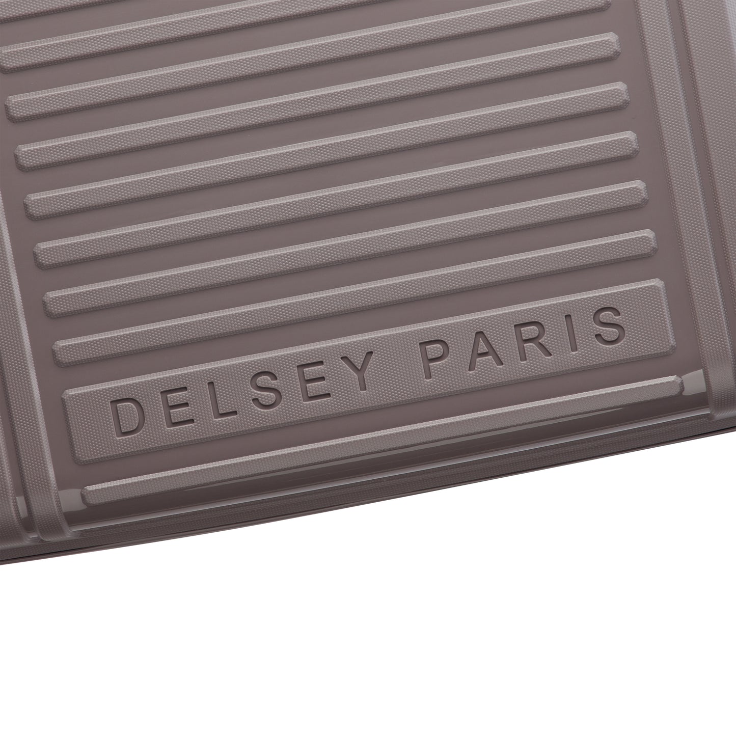 Detalhe em close da superfície texturizada de mala de viagem DELSEY em tom castanho claro, destacando design resistente e elegante com gravação da marca DELSEY PARIS.