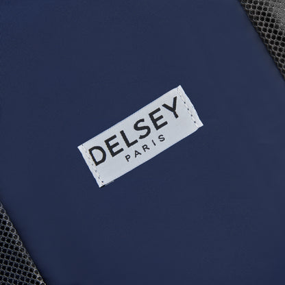 Etiqueta branca com a marca DELSEY Paris costurada em tecido azul escuro, parte de um kit organizador de viagem com acabamento em malha preta, representando acessório premium para mala de viagem.