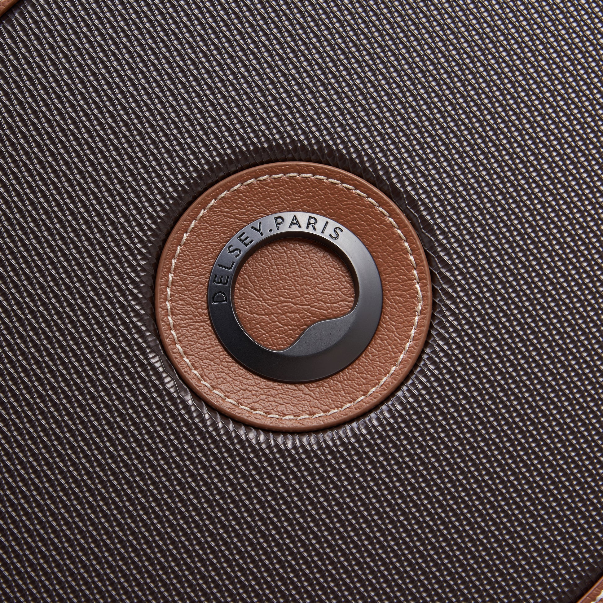 Close-up do logo da marca DELSEY Paris em mala de viagem média na cor chocolate com textura fina e detalhes em couro marrom.
