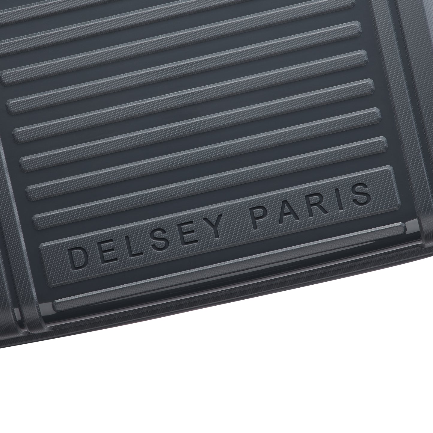 Detalhe da parte frontal cinza escuro de mala de bordo rígida com textura em linhas horizontais e logo DELSEY PARIS em relevo, destacando design e durabilidade.
