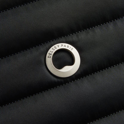 Detalhe do logo metálico da DELSEY Paris aplicado sobre tecido preto em textura acolchoada, representando a qualidade e design premium da marca.