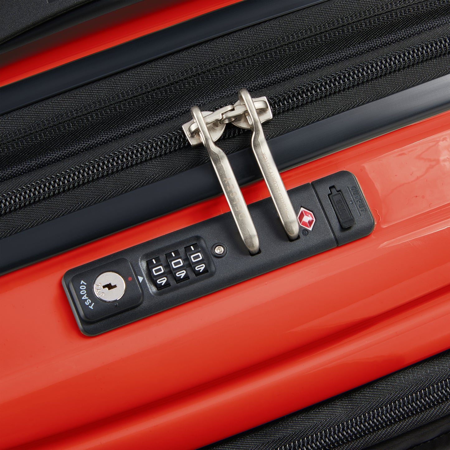 Fecho com zíper antifurto e trava TSA em mala rígida laranja expansível da DELSEY, ideal para viagens seguras com compartimento para notebook.