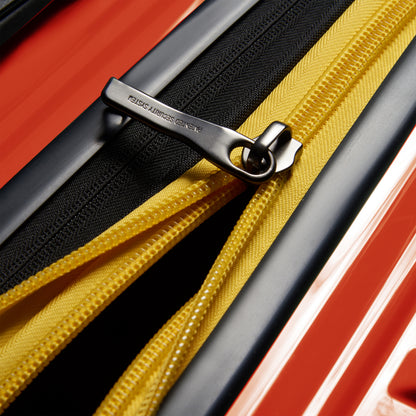 Fecho de zíper reforçado preto e amarelo em mala rígida laranja, destacando design resistente e inovação da DELSEY, ideal para viagens seguras e duráveis.