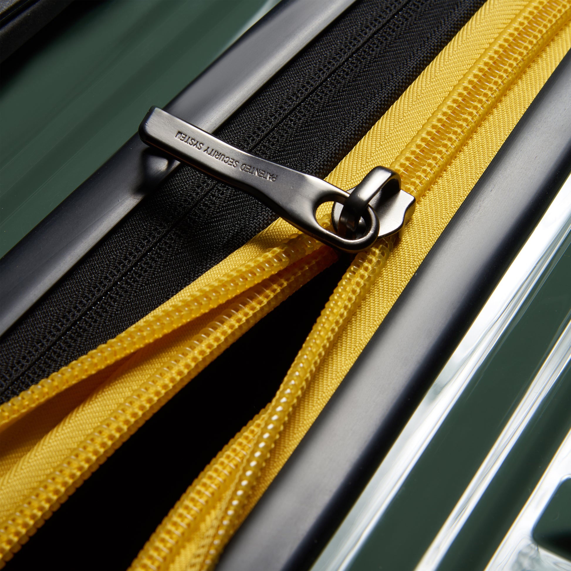 Fechadura metálica de zíper antifurto em mala rígida verde com detalhe amarelo, destacando acabamento premium da DELSEY.