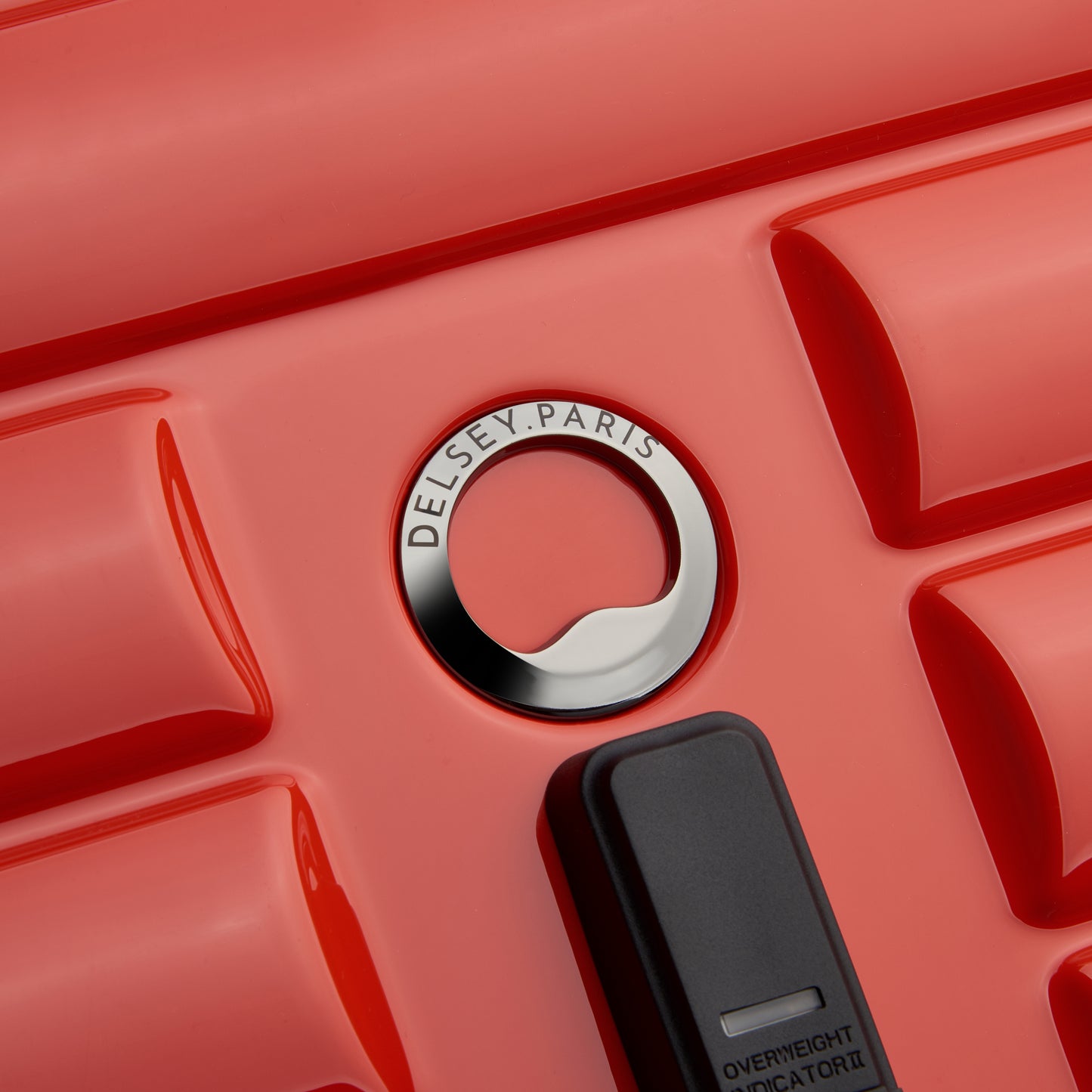 Detalhe da superfície rígida e texturizada de mala de viagem laranja, com logo em metal da DELSEY Paris, destacando design e qualidade premium.