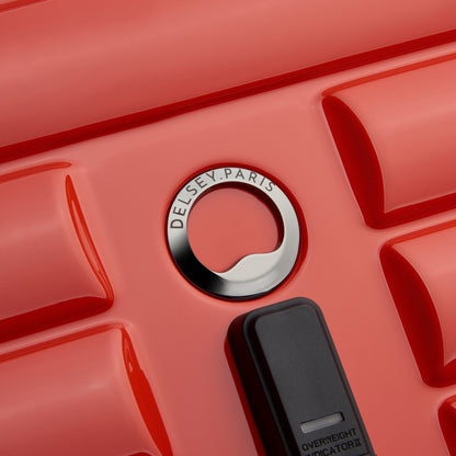 Detalhe da superfície rígida e texturizada de mala de viagem laranja, com logo em metal da DELSEY Paris, destacando design e qualidade premium.