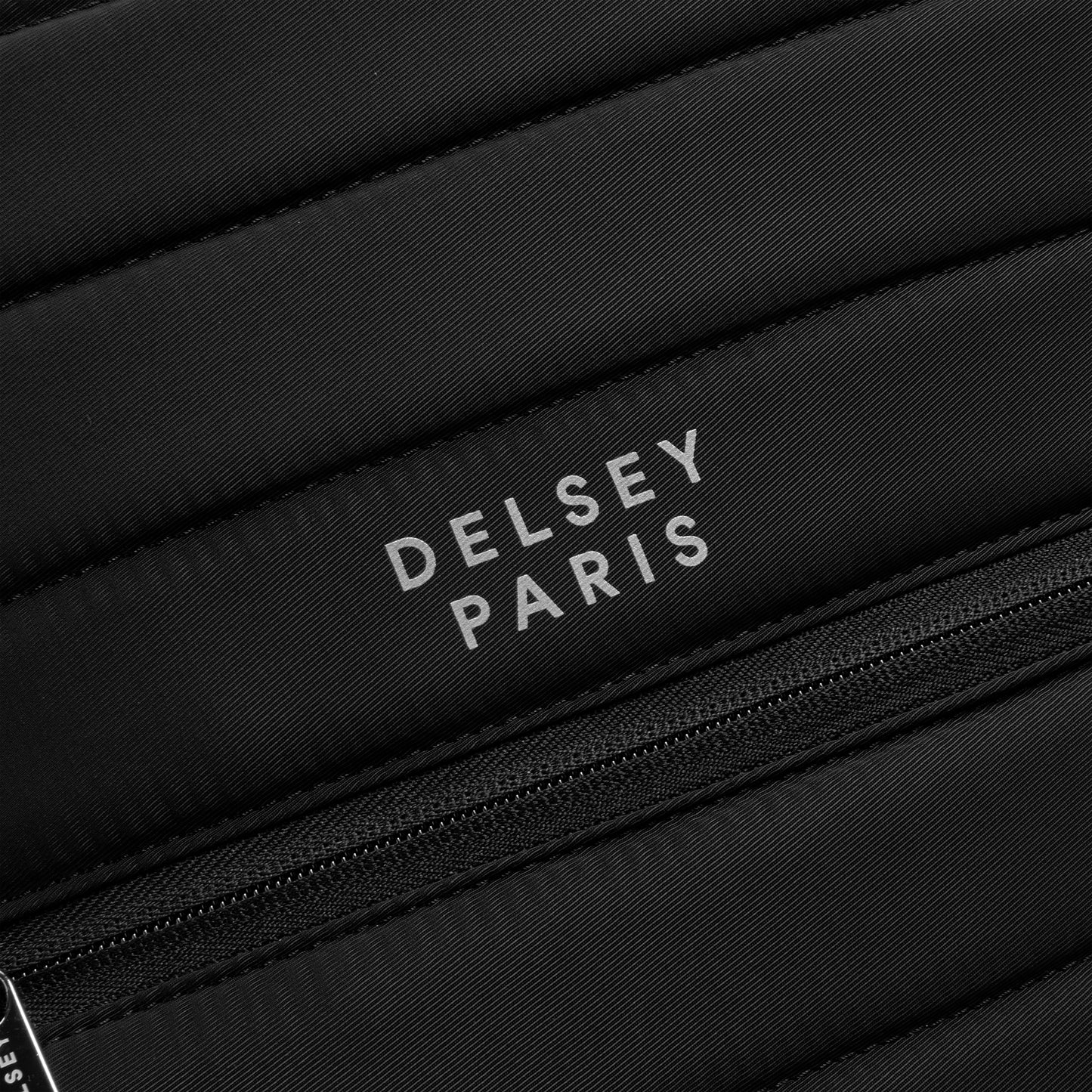 Logo da marca DELSEY Paris em mochila preta com textura acolchoada e zíper, representando acessórios de alta qualidade para notebook e viagem.