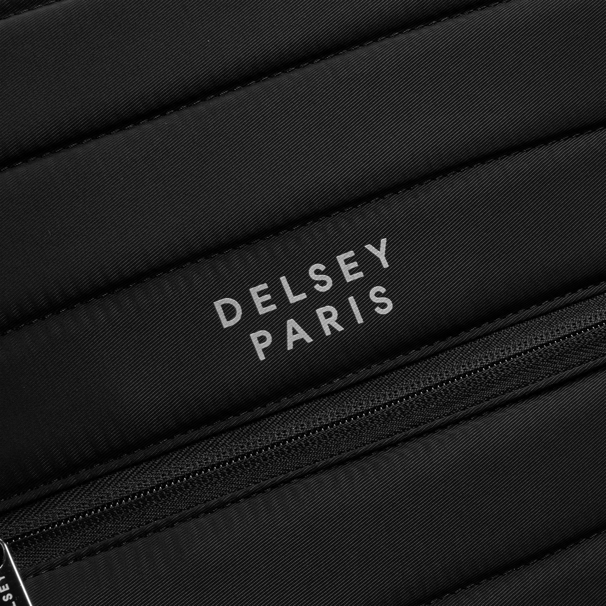 Logo da marca DELSEY Paris em mochila preta com textura acolchoada e zíper, representando acessórios de alta qualidade para notebook e viagem.