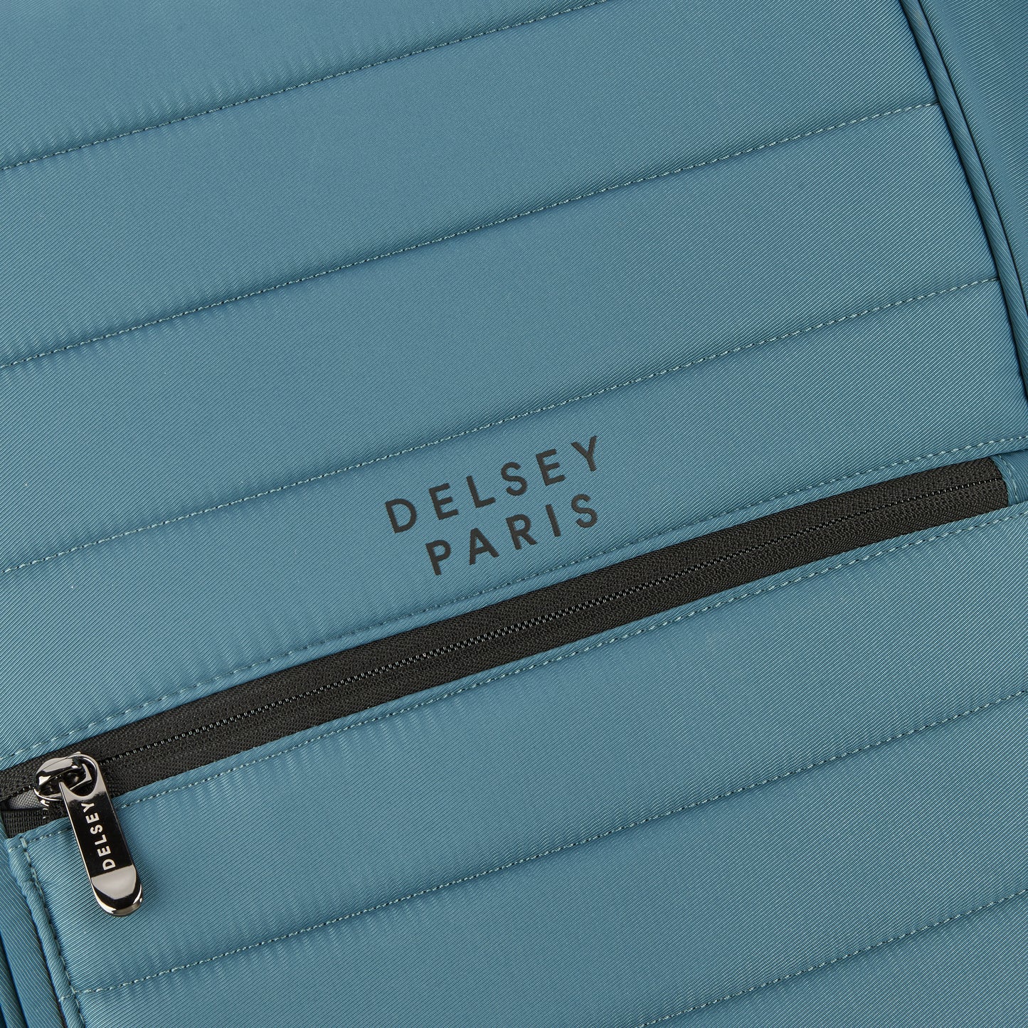 Detalhe em close de mochila DELSEY Paris em tecido resistente azul com zíper preto e costura reforçada, exemplificando qualidade e design premium.