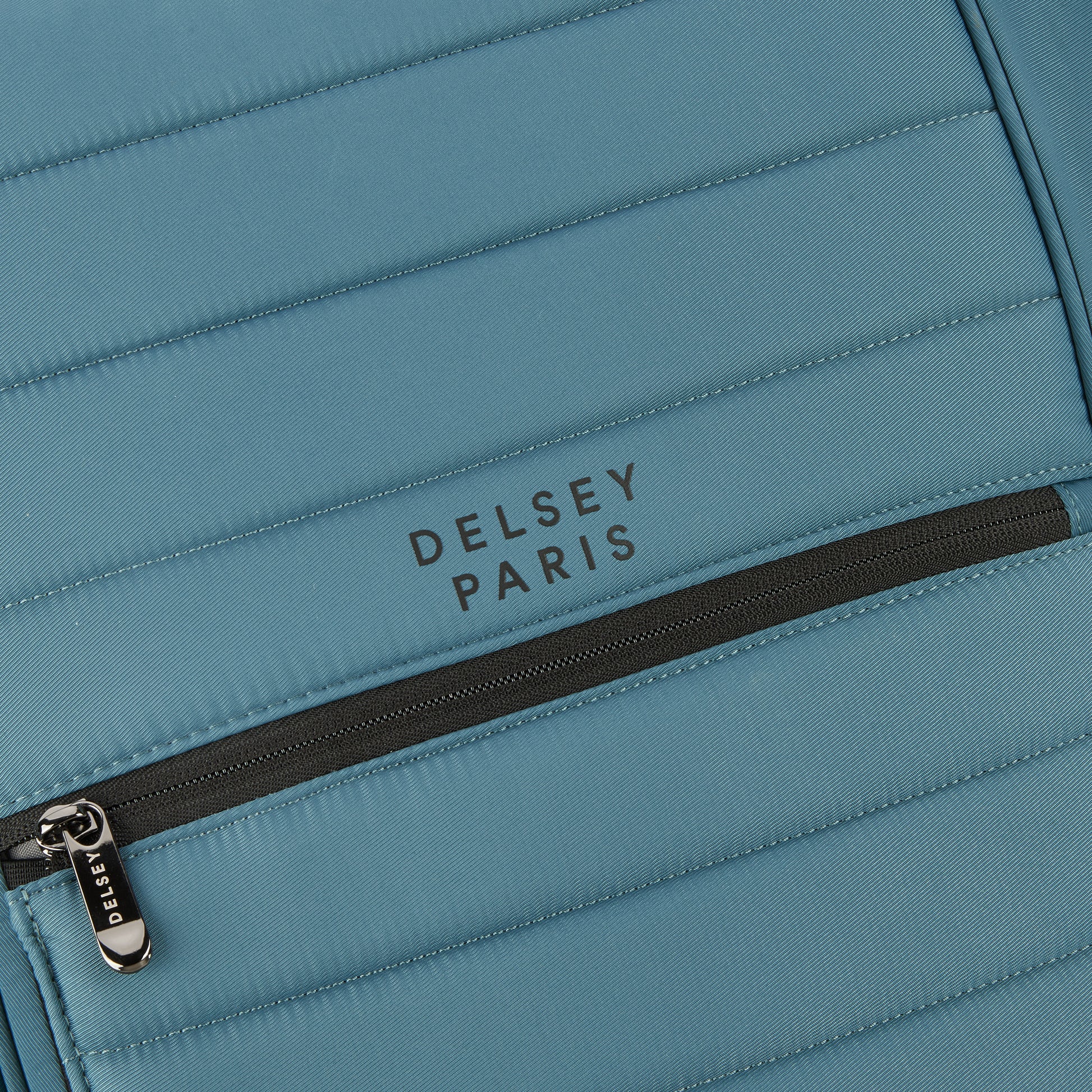 Detalhe em close de mochila DELSEY Paris em tecido resistente azul com zíper preto e costura reforçada, exemplificando qualidade e design premium.
